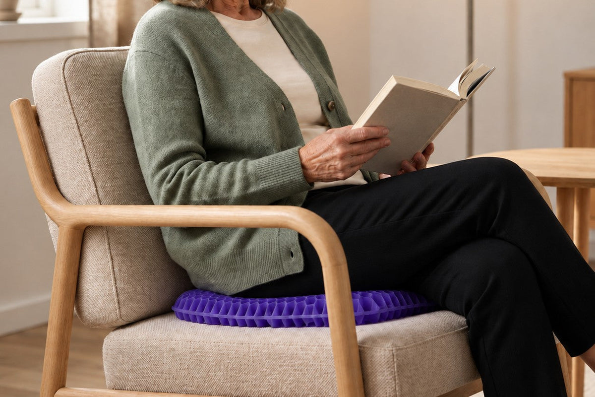 Kvinna läser en bok i en fåtölj och sitter på den lila sittkudden ErgoGel Pro