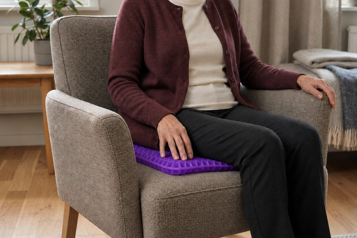 Kvinna i vinröd kofta sitter i en grå fåtölj på en lila sittkudde i gel